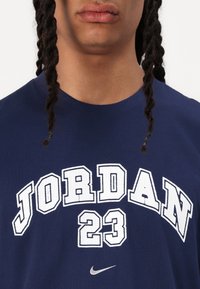 Námořnická modrá bavlněná tričko s nápisem "JORDAN 23" v bílých, tučných písmenech přes hruď a malým stříbrným logem Nike swoosh.