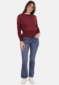 Maglione a coste color bordeaux con una finitura testurizzata e orlo a costine, abbinato a jeans blu attillati e scarpe da ginnastica bianche.