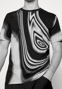 Camiseta de manga corta en negro y gris con un patrón de olas en espiral. Cuello redondo clásico y tejido suave, forma ajustada, superficie texturizada.