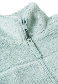 Mintgrön fleecetröja med hög krage, som har dragkedja med en texturerad dragflik. Mjuk, fluffig yta.