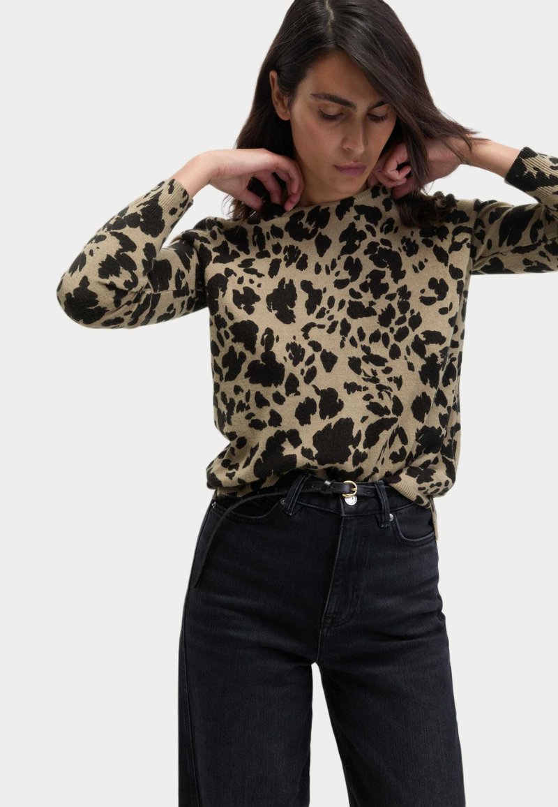 Maglione lavorato a maglia color beige con stampa leopardata nera, dotato di scollo rotondo e maniche lunghe, abbinato a jeans neri a vita alta.