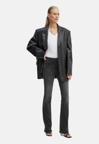 Blazer oversize in pelle nera sovrapposto a una t-shirt bianca a scollo a V, abbinato a jeans grigi scuri a campana e sandali neri.