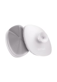 Witte silicone gezichtsreinigingsapparaat met textuur oppervlakten, een ronde vorm en een centrale zuignap voor grip. Gegraveerde merknaam "GESKE."