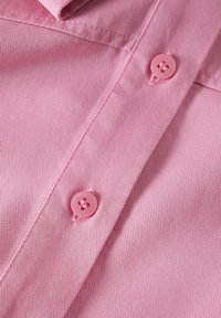Tessuto rosa con una texture a coste che presenta due bottoni rotondi cuciti. Il colletto e la patta dei bottoni sono visibili nell'angolo.