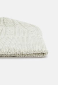 Beanie lavorato a maglia color crema con texture a coste e motivo a treccia, piegato sul bordo. Realizzato in morbido materiale misto lana caldo.