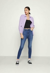 Camisa oversized de lavanda, top cropped preto, jeans skinny azuis e ténis pretos. Tecido suave e design ajustado com estilo clássico.