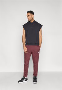 Juodas be rankovių gobtuvu megztinis su priekyje esančiu logotipu, derinamas su bordo spalvos sportinėmis kelnėmis. Kelnių šlaunyje yra logotipas, vilkimos su juodais sportiniais bateliais.