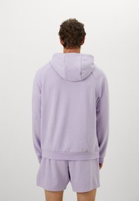 Lilla hettegenser med buet kant og justerbar hette, kombinert med matchende shorts. Stoffet ser mykt ut med et enkelt, rent design.