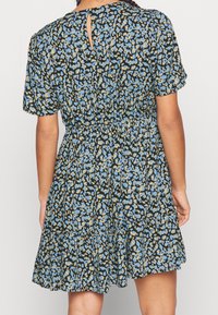 Vestido de estampado floral en negro, azul y amarillo. Mangas cortas, cintura entallada, falda de capas, con abertura en la espalda tipo ojal. Textura de tela suave.