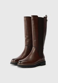 Καφέ δερμάτινες μπότες μέχρι το γόνατο με ελαστικές πλαϊνές επενδύσεις, στρογγυλή μύτη, υφή και παχύ μαύρο λαστιχένιο πάτο.