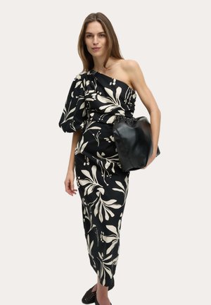 Sort blomsterkjole med hvide bladmønstre, ét skulderdesign, puffede ærmer, kombineret med en sort læderhåndtaske og flade sko.