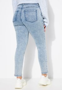 Jeans ajustados de color azul claro con una textura de denim deslavado, que presentan una cintura de altura media y dos bolsillos traseros. Acompañados de zapatillas blancas.