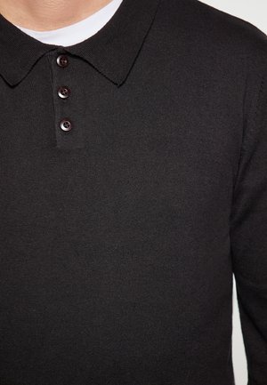 Černé pletené polo tričko s klasickým límcem, třemi tmavými knoflíky a hladkou texturou. Má vrstvený design s bílou vnitřní košilí.