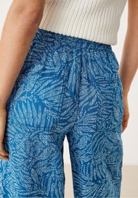 Sinisävyiset kuviolliset housut pehmeästä kankaasta, joissa on joustava vyötärönauha ja monimutkaiset valkoiset lehtimäiset kuviot. Takakuvassa näkyvät taskujen yksityiskohdat.