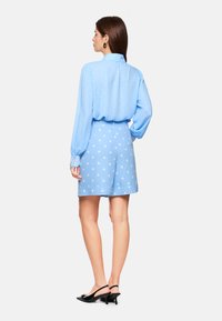 Light blue blouse with polka dots, long sleeves, and a collar, paired with light blue polka dot shorts; black heeled shoes complete the outfit.