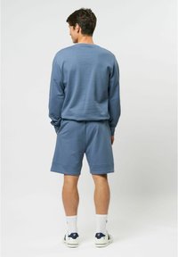 Blauwe sweatshirt en short set gemaakt van zachte stof. De sweatshirt heeft een ronde hals, en de shorts hebben wijde pijpen met geribbelde manchetten. Witte sneakers en sokken.