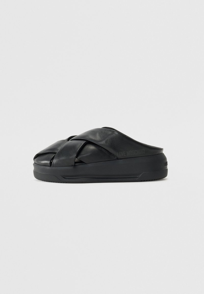 Czarne klapki mają skrzyżowany wzór pasków wykonany z gładkiej skóry oraz grubą czarną gumową podeszwę z subtelnym logo.
