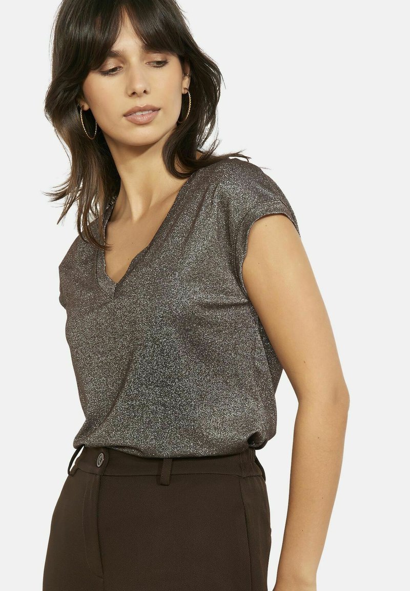 Top di bronzo lucido con scollo a V e maniche corte, tessuto leggermente strutturato, abbinato a pantaloni su misura marrone scuro. Effetto leggermente brillante.