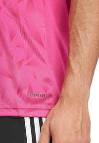 Roze T-shirt met korte mouwen, voorzien van een gestructureerd patroon, AEROREADY-merk en een gladde stof. Zwarte accenten aan de onderkant.