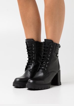 Black leather lace-up ankle boots with a chunky high heel, rounded toe, and rugged tread sole; features silver eyelets and ribbed accents.