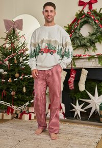 Šedá mikina s červeným náklaďákom a stromami, v kombinácii s červenými a bielymi károvanými pyžamovými nohavicami. Umiestnené v slávnostnej miestnosti s vianočnými dekoráciami.