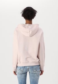 Sudadera de algodón rosa con una gran capucha, puños y dobladillo acanalados. La vista trasera revela un diseño simple sin adornos adicionales.