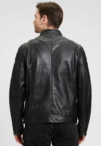 Zwarte leren jas met een getailleerd ontwerp, voorzien van doorgestikte schouderaccenten en ritsmanchetten. Gladde textuur met een matte afwerking.