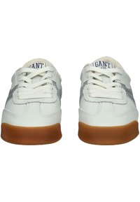 Bílé kožené tenisky s šedými akcenty, plochými tkaničkami, kulatou špičkou a gumovou podešví. Název značky viditelný na jazyku. Klasický design.