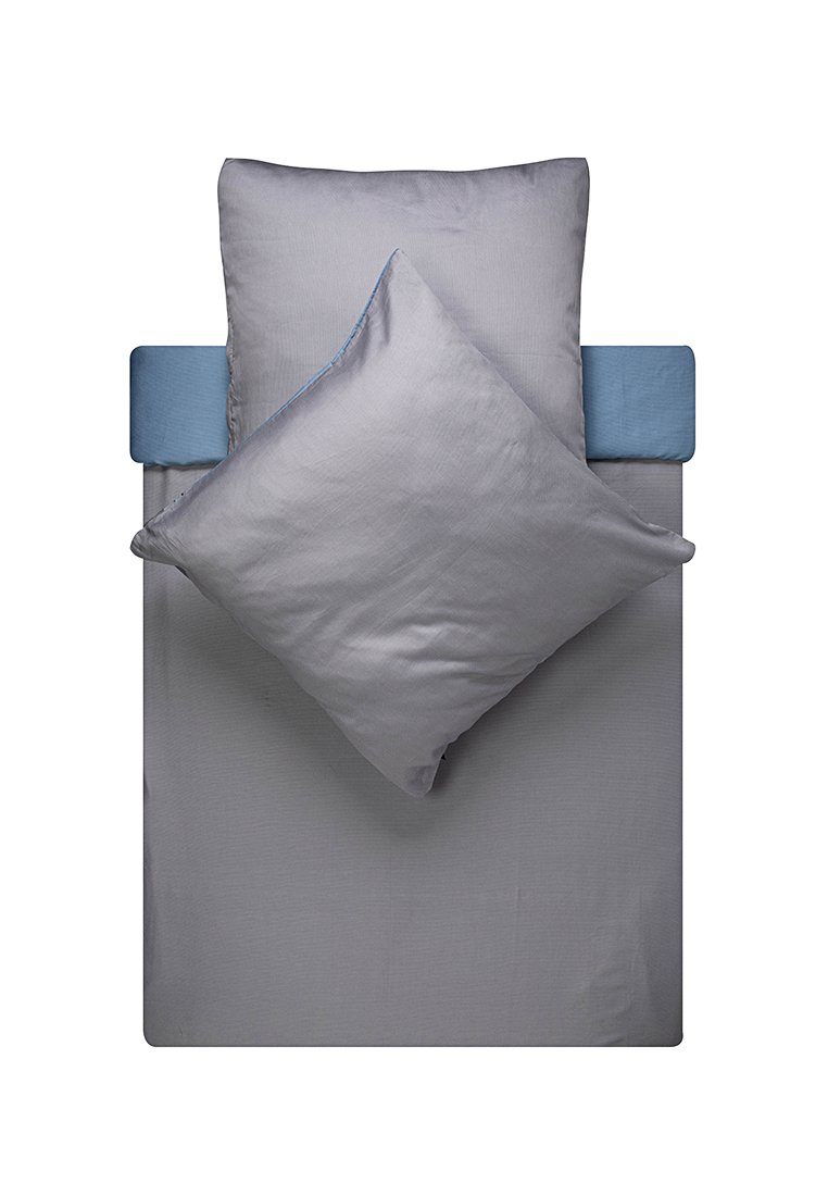 Ein Einzelbett mit einem grauen Spannbettlaken, zwei grauen Kissen – eines schräg platziert – und einem blauen Bolsterkissen am Kopfende.