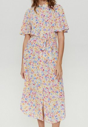 Woman wearing a yellow short-sleeve floral dress with button-down front and a tied waist belt against a plain background.