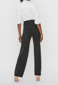 Pantalones de pierna ancha de talle alto en tejido de punto gris oscuro, con una textura suave y bordes terminados, combinados con una camisa blanca de botones.