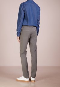 Šedé kalhoty slim fit s dvěma zadními kapsami se stříbrným prošíváním. Doplněno modrou džínovou košilí a bílými teniskami.