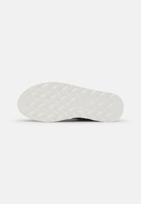 Suela negra de zapato con una parte inferior de goma blanca texturizada que presenta un patrón de zigzag, diseñada para ofrecer agarre y tracción.