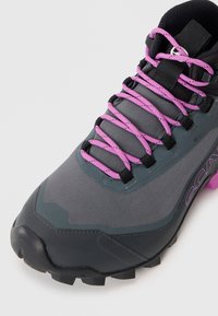 Grauer Wanderschuh mit strukturiertem Obermaterial, schwarzen Akzenten und leuchtend pinken Schnürsenkeln. Auffällige, robuste Sohle für Traktion und Unterstützung.