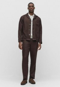 Brun linjacka med notchkräg och bröstficka, i kombination med matchande byxor. Har knappar och en texturerad tygfinish.