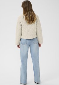 Giacca beige trapuntata con cuciture diagonali, design cropped e maniche lunghe abbinata a jeans a gamba larga di un blu chiaro.