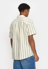 Korte mouw shirt in lichtbeige met verticale marineblauwe strepen. Beschikt over een puntkraag en een relaxte pasvorm, gemaakt van lichtgewicht katoen of linnen.