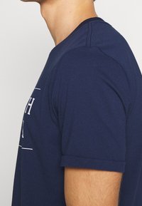 Granatowa koszulka bawełniana z okrągłym dekoltem, krótkimi rękawami i dopasowanym krojem. Na przodzie wyświetlona grafika tekstowa.