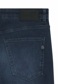 Jeans av denim i mörkblått med en läderetikett från BOSS vid midjan. Har en bakficka med en liten märkesdetalj.