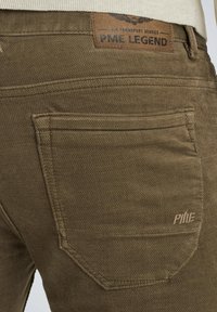 Brązowe bawełniane spodnie z teksturowanej tkaniny, charakterystycznym stębnowaniem tylnych kieszeni i skórzaną metką oznaczoną "PME LEGEND."