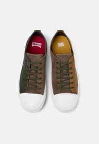 Brune ruskind sneakers med grønne læderdetaljer, olivenfarvede snørebånd og hvid gummi tåhætte. Indersåler i rød og gul, mærket "CAMPER" og "TWINS."