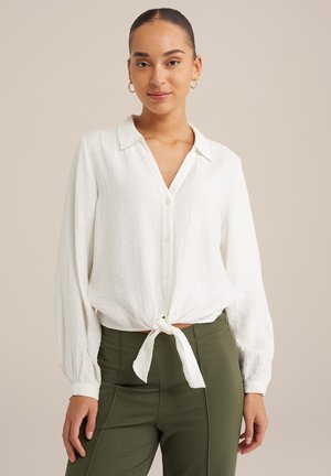Witte, lichte, knoopsluiting shirt met een kraag en lange mouwen, knoopte in de taille; gecombineerd met olijfgroene, strakke broek.