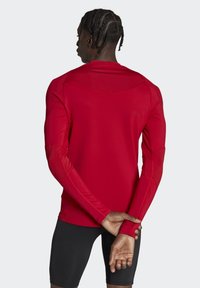Rotes Langarm-Sportshirt mit glatter Textur, enganliegendem Design und kontrastierenden orangen Nähten. Entwickelt für aktive Nutzung.