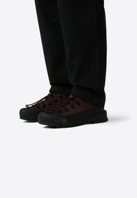 Tumman viininpunaiset vaelluskengät, joissa on teksturoitu verkko-osa ja musta kumipohja. Varusteena nauhakiinnitys ja The North Face -logo sivulla.