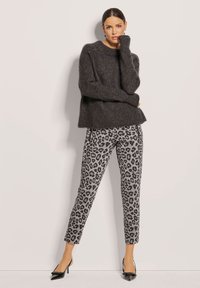 Donkergrijze wollen trui met een oversized pasvorm, gecombineerd met grijze broek met luipaardprint en zwarte pumps met spitse neus. Eenvoudig, modern ontwerp.