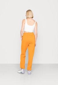 Orange mjukisbyxor med en avslappnad passform och elastisk midja, kombinerat med en vit ribbad crop top. Skorna har ljuslila detaljer.