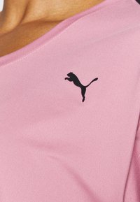 Růžový sportovní top z hladké látky, s výstřihem do V a černým logem Puma na levé straně hrudníku.