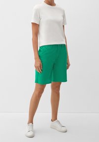 Shorts en coton vert à coupe droite avec deux poches latérales, assortis à un t-shirt blanc uni à manches courtes et des baskets blanches.