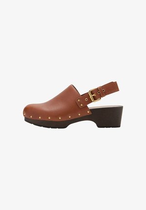 Sabot en cuir marron avec des clous dorés, une boucle dorée et une semelle talon noire épaisse.