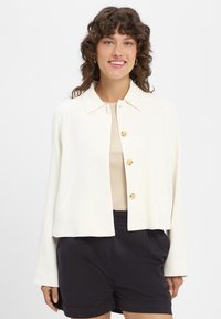 Crèmekleurig jack met kraag, vier ronde knopen, zijzakken en lange mouwen. Gladde textuur met een relaxte pasvorm.